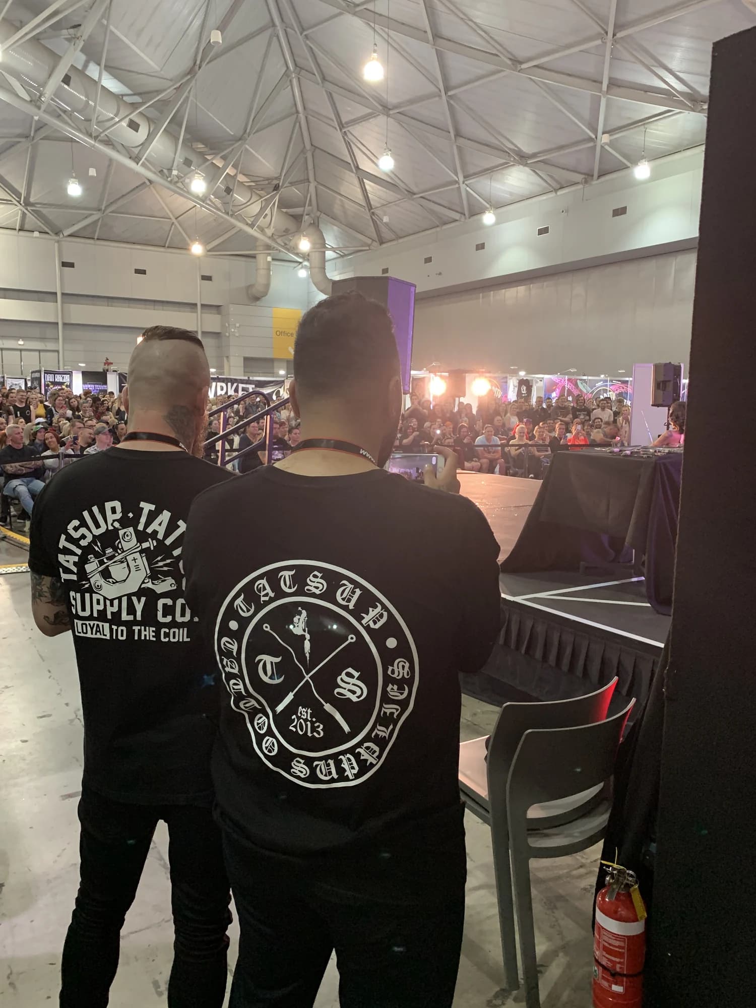 Kevin Mack seen from behind in a staff shirt, looking out over a busy exhibition hall