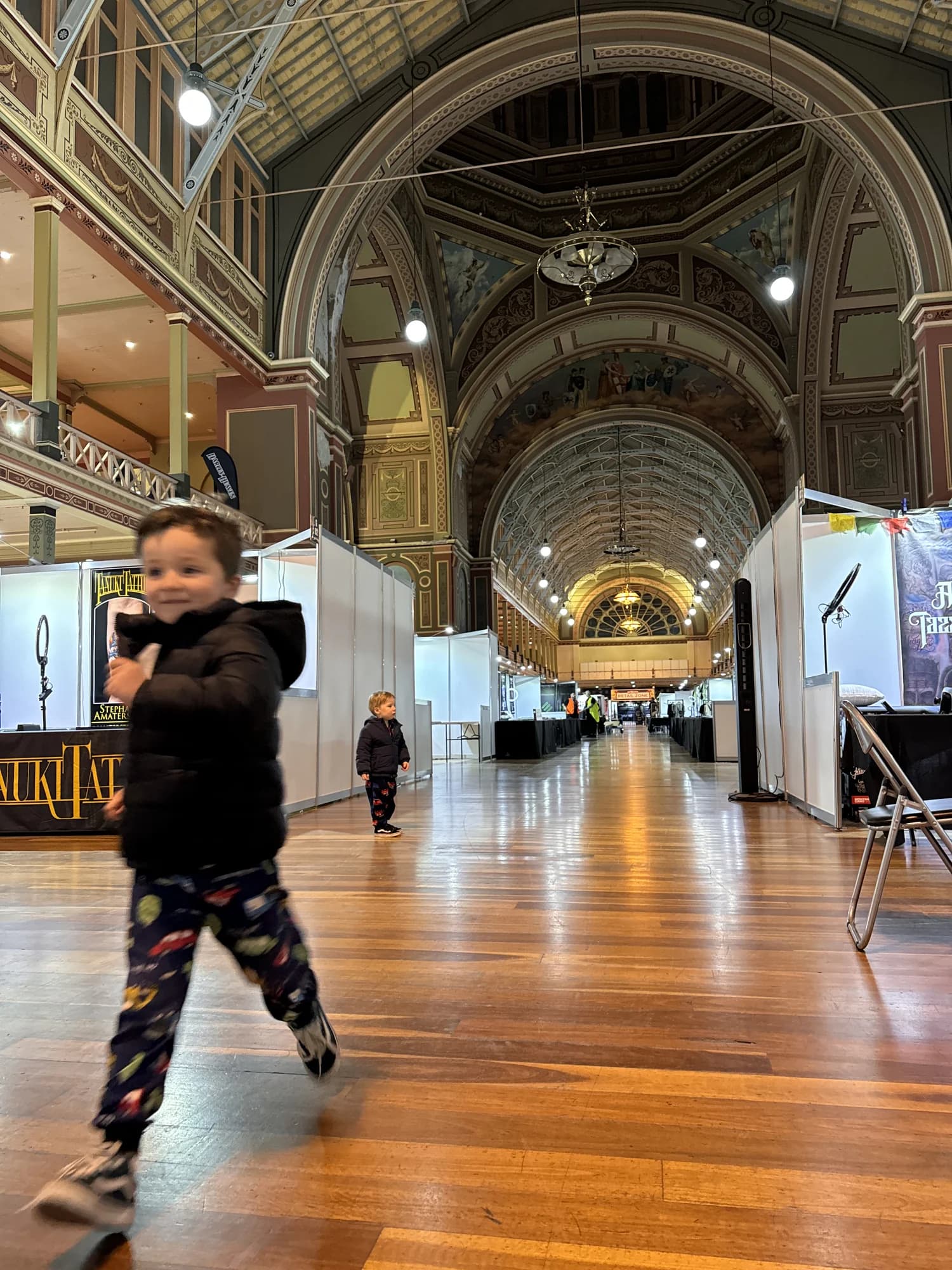 A small boy running down the hall of the Royal Exhibition Building between exhibition stands