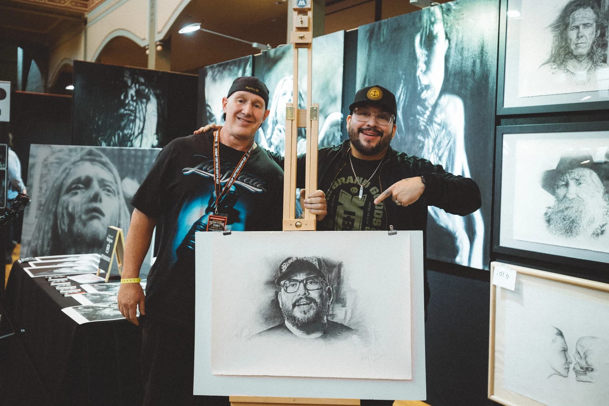 Kevin Mack with an artist beside framed portrait drawings